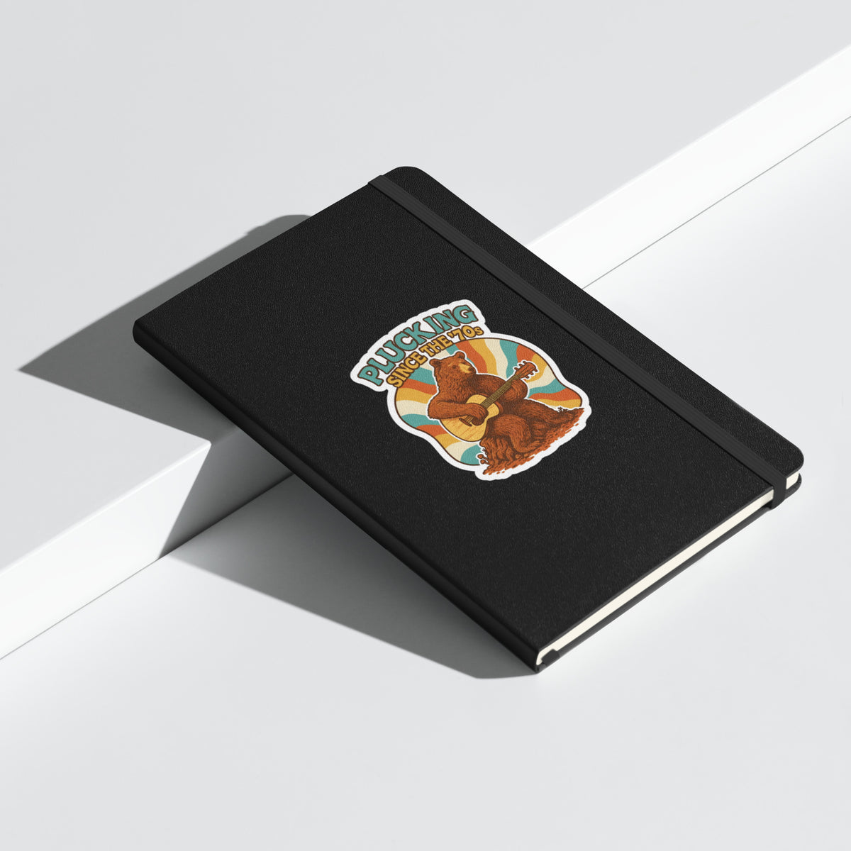 Plucking Since the 70s Retro Bear Guitar Hardcover Notebook - Black angled closed mockup