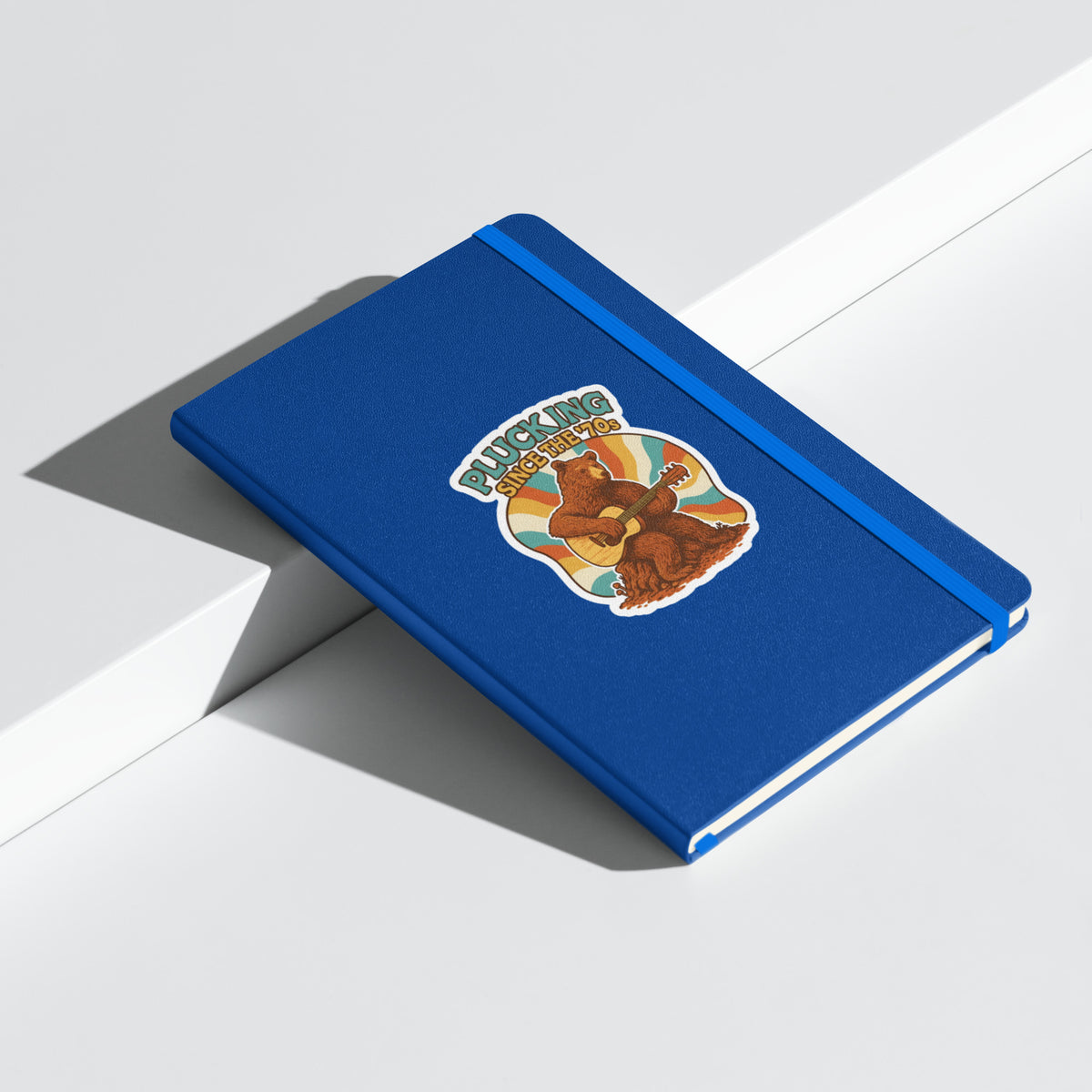 Plucking Since the 70s Retro Bear Guitar Hardcover Notebook - Blue angled closed mockup