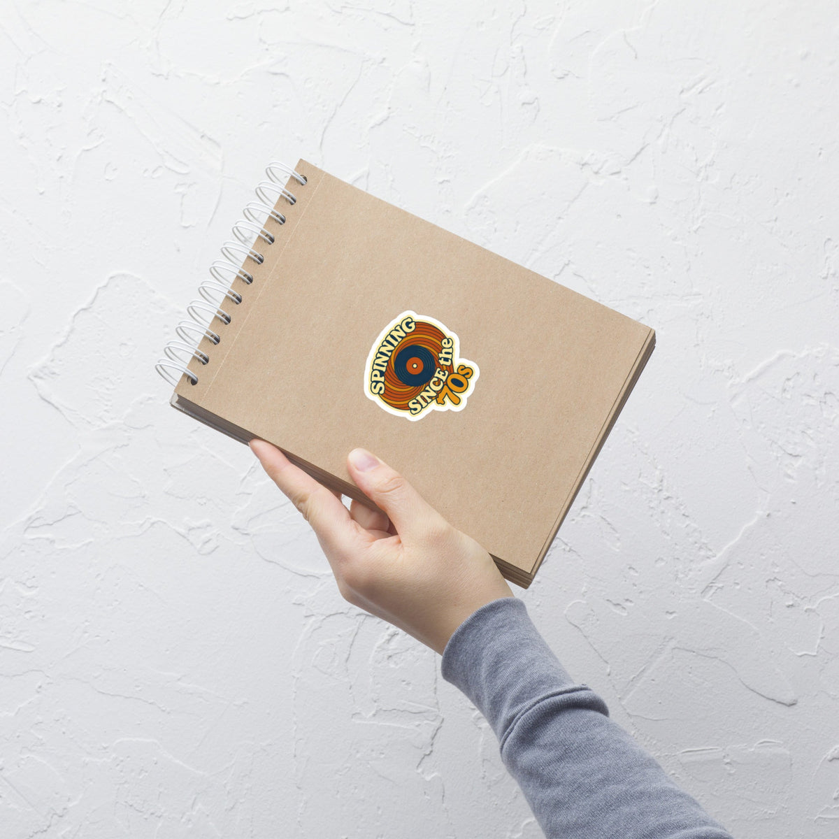 Spinning Since the 70s Music Sticker on a notebook held by hand